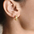 Gold sunburst hoop earring worn on an earlobe, showing the wide band and repeating radiant pattern.