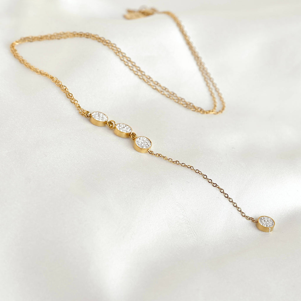 Gold pavé circle lariat necklace arranged on white fabric, showing the fine chain, three linked crystal circles and long pendant drop.