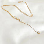 Gold pavé circle lariat necklace arranged on white fabric, showing the fine chain, three linked crystal circles and long pendant drop.