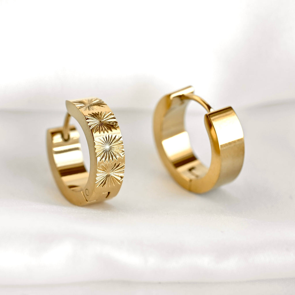 Front and rear views of gold sunburst hoops on a white surface, showing the patterned band and polished back.