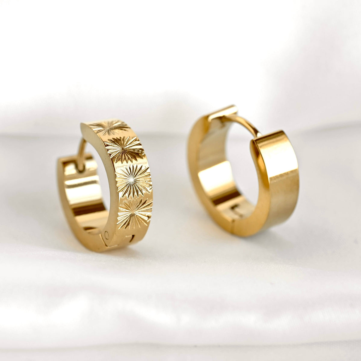 Front and rear views of gold sunburst hoops on a white surface, showing the patterned band and polished back.