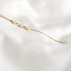 Close-up of a gold lariat necklace on white fabric, showing pavé crystal circles and the chain leading to the final round drop.