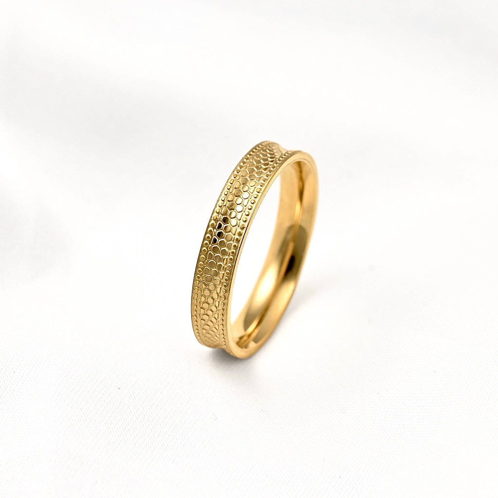 Gold concave stacking ring standing upright on a white surface, showing its snake-inspired texture and raised edges.