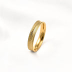 Gold concave stacking ring standing upright on a white surface, showing its snake-inspired texture and raised edges.