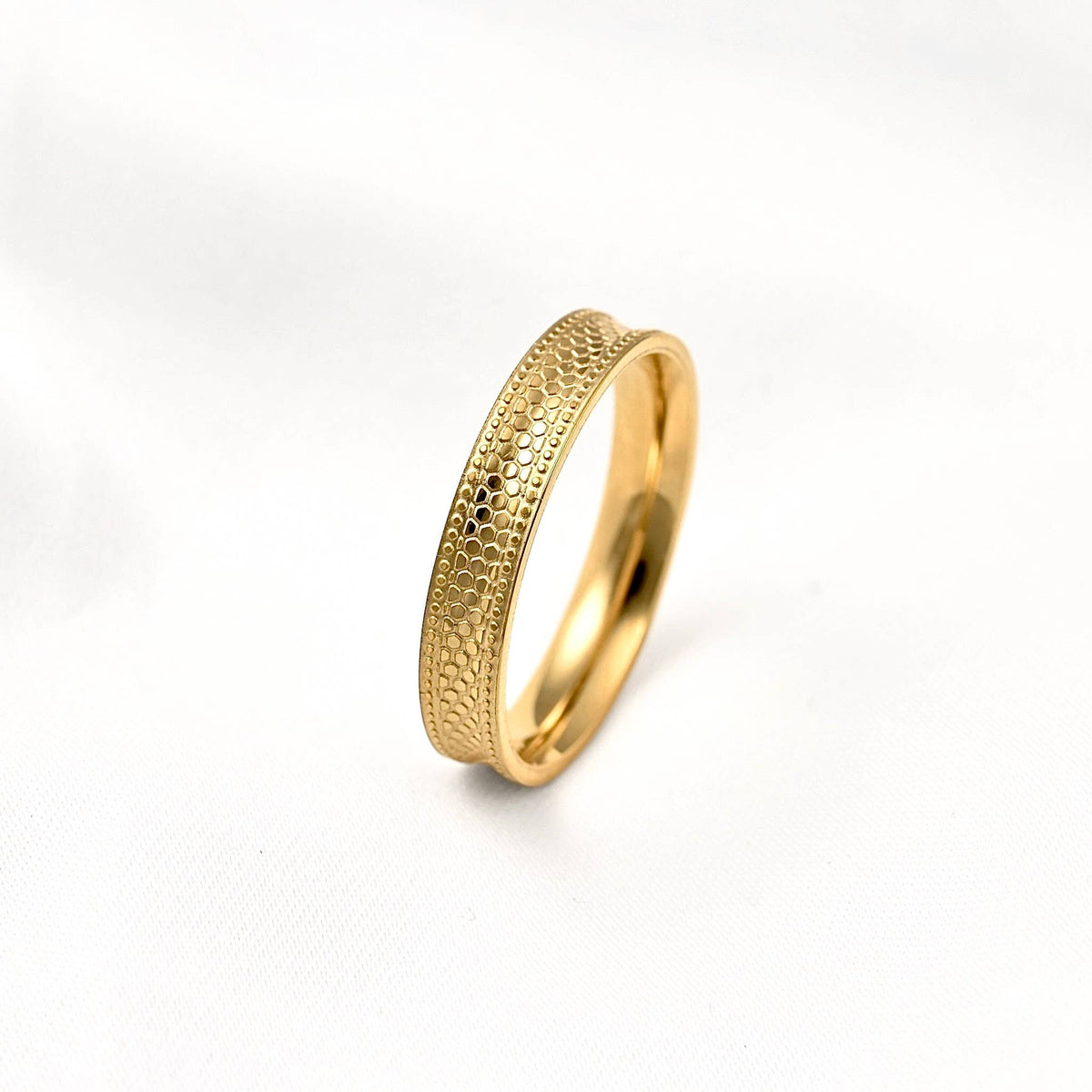 Gold concave stacking ring standing upright on a white surface, showing its snake-inspired texture and raised edges.