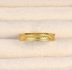 Front detail of the gold stacking ring in a cream jewellery tray, showing the repeating textured pattern.