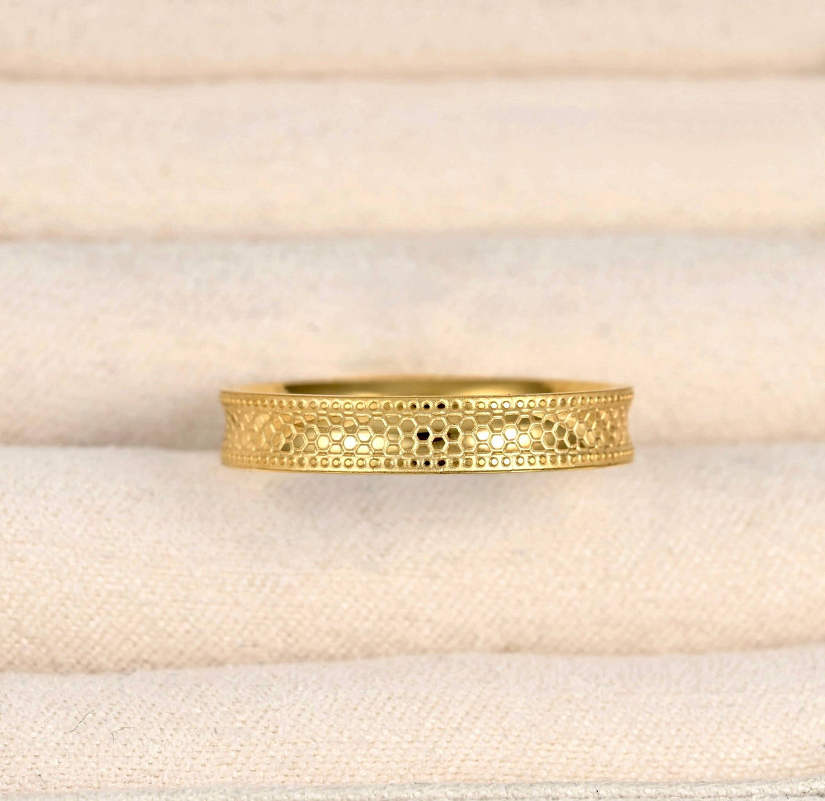 Front detail of the gold stacking ring in a cream jewellery tray, showing the repeating textured pattern.
