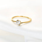 Gold bypass solitaire ring lying on a white surface, showing the slender band curving around a round clear stone.