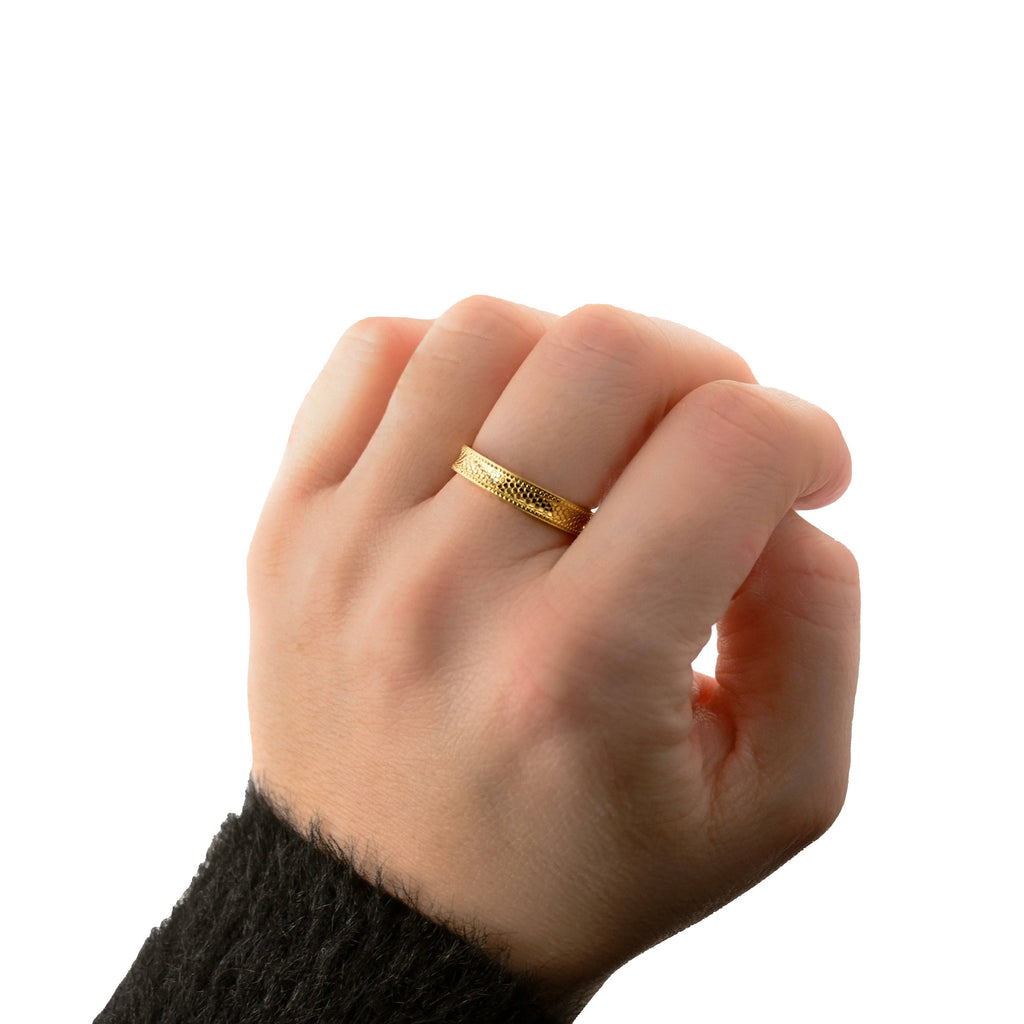 Gold textured stacking ring worn on a hand with a dark knit sleeve against a white background.