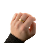 Gold textured stacking ring worn on a hand with a dark knit sleeve against a white background.