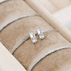 Pair of clear rectangular bar stud earrings with silver-tone settings displayed in a cream jewellery tray.