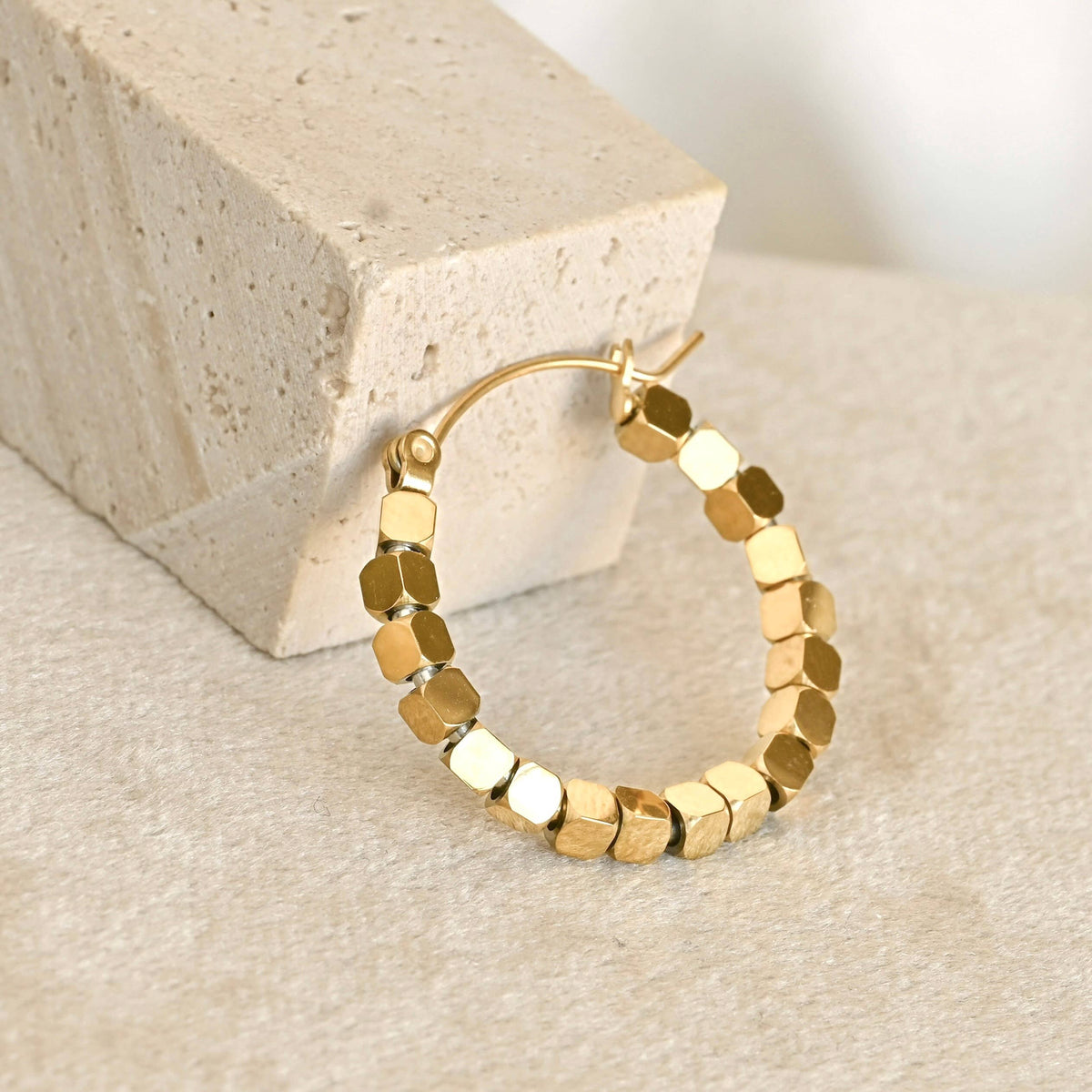 Single gold cube bead hoop earring beside a cream stone block, showing the wire closure