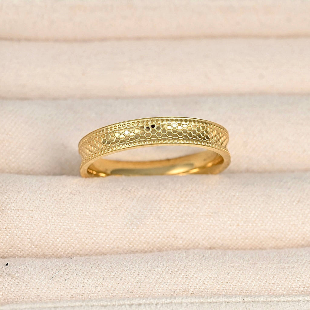Close-up of the gold ring in a cream jewellery case, highlighting the textured concave band and dotted borders.