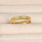Close-up of the gold ring in a cream jewellery case, highlighting the textured concave band and dotted borders.