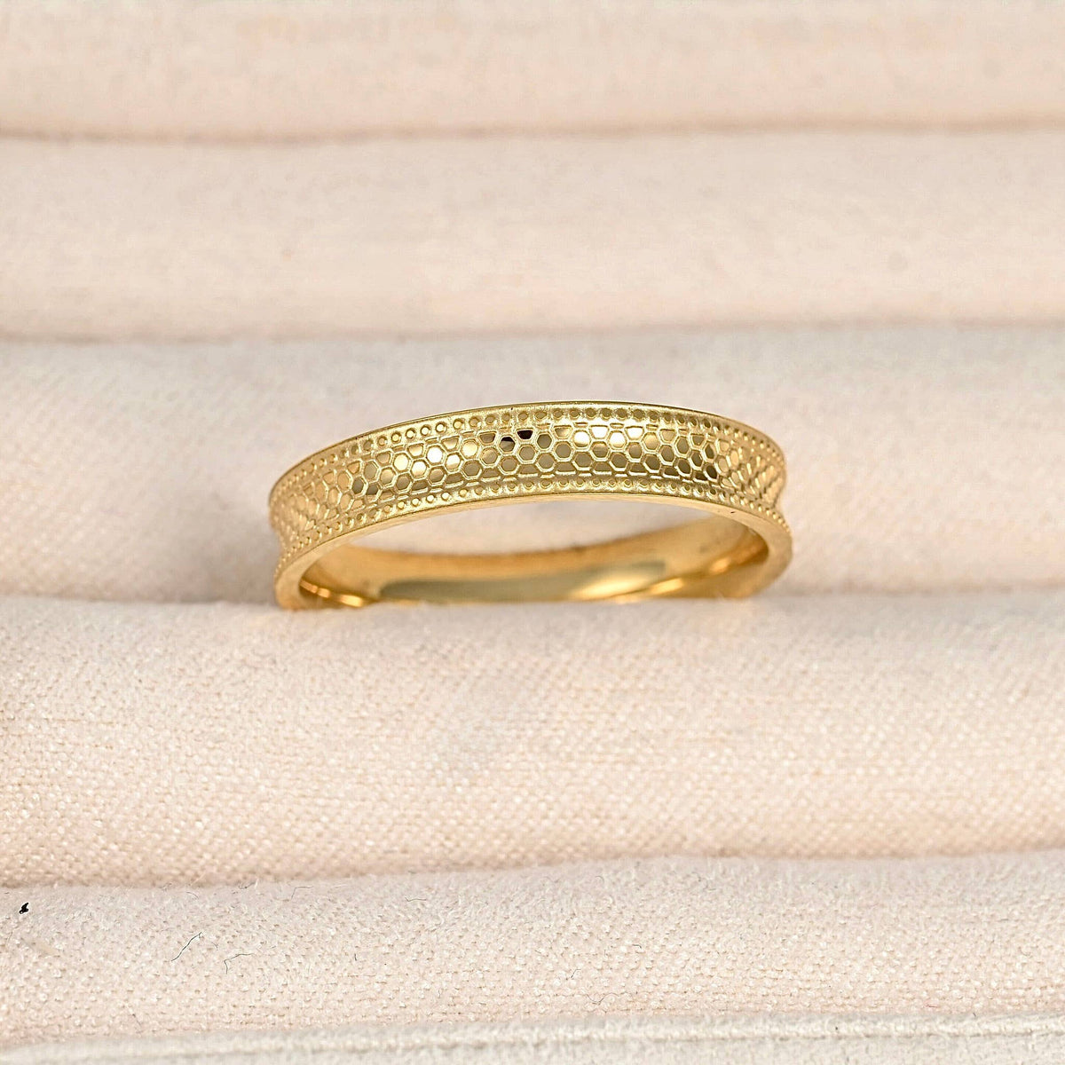 Close-up of the gold ring in a cream jewellery case, highlighting the textured concave band and dotted borders.