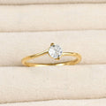 Close-up of a gold bypass solitaire ring with a round clear stone and curved polished band in a cream jewellery tray.