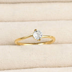 Close-up of a gold bypass solitaire ring with a round clear stone and curved polished band in a cream jewellery tray.