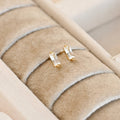 Pair of clear baguette-style bar studs with gold-tone settings displayed in a cream jewellery tray.