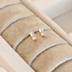 Pair of clear baguette-style bar studs with gold-tone settings displayed in a cream jewellery tray.