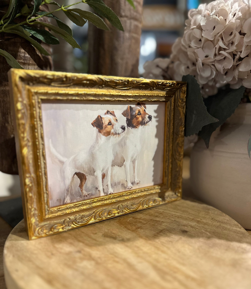 Jack Russel artwork featuring two white and brown terriers in an ornate gold frame, displayed on a wooden board beside white hydrangeas.