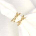 Front view of gold-tone criss cross hoop earrings on white fabric, highlighting the clear stones and X-shaped design.