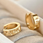 Close-up of gold sunburst hoop earrings in a cream jewellery tray, highlighting the engraved-style radiant detailing.