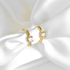 Gold-tone huggie hoop earrings with single round clear stones, displayed on folded white satin.