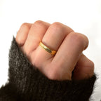 Close-up of the gold textured stacking ring worn on a hand beside a dark knit cuff.