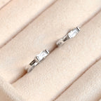 Pair of silver-tone huggie earrings with rectangular clear stones in a cream jewellery tray.