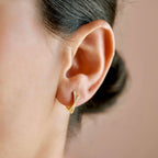 Gold-tone pavé criss cross hoop earring worn on an earlobe, showing the crossed stone-set rows.