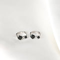 Pair of Blueyejewelry sterling silver huggie hoop earrings, each featuring one large and one small black stone, on a white surface.