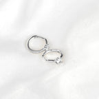 Silver-tone huggie hoop earrings with round clear stones resting on white fabric, showing hinged closures.